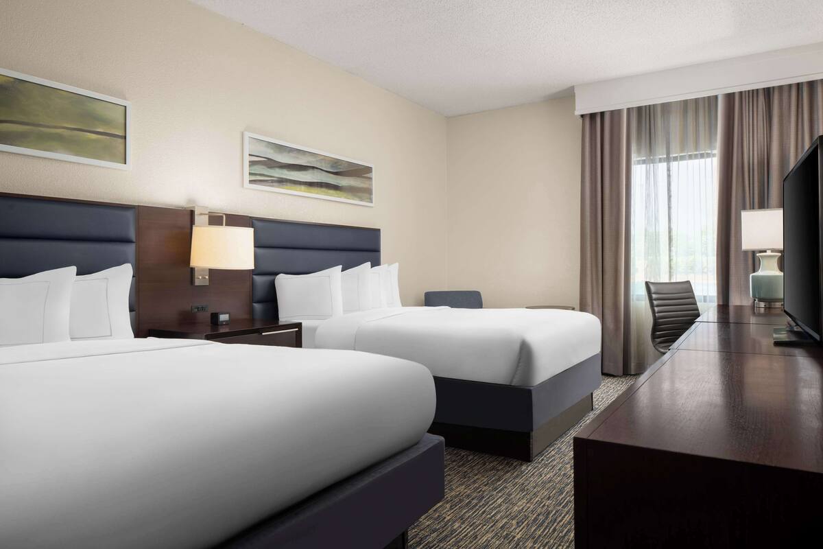 A hotel room with two beds, a desk, a TV, and a window with curtains.