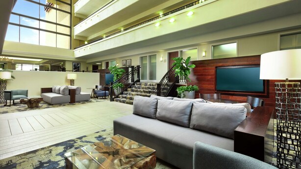 A spacious lobby with a high ceiling, a staircase, a large sofa, a coffee table, and a TV mounted on the wall. - Doubletree by Hilton Columbia, SC (Columbia)