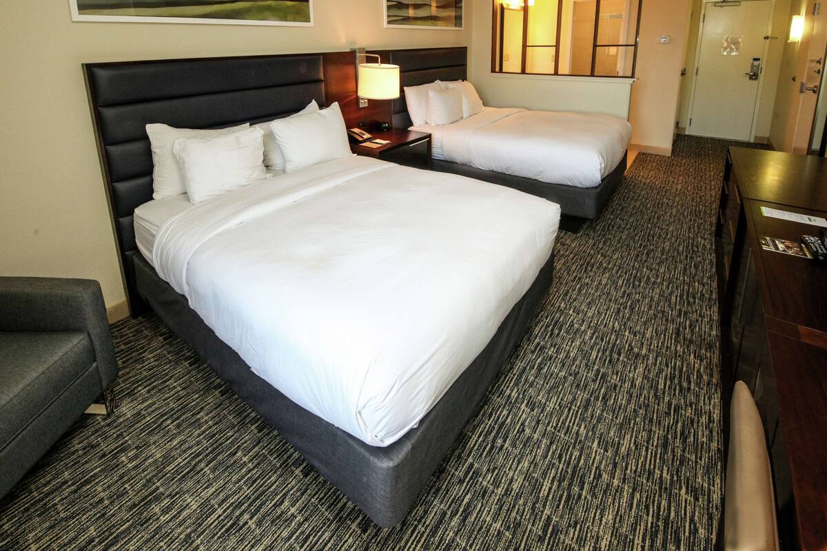 A hotel room with two beds, a desk, a chair, and a carpeted floor.