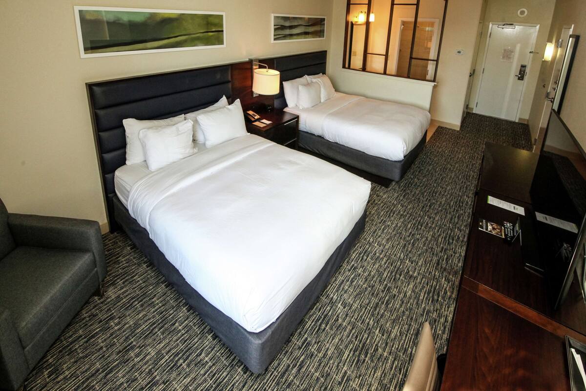 A hotel room with two beds, a desk, a chair, and a TV.