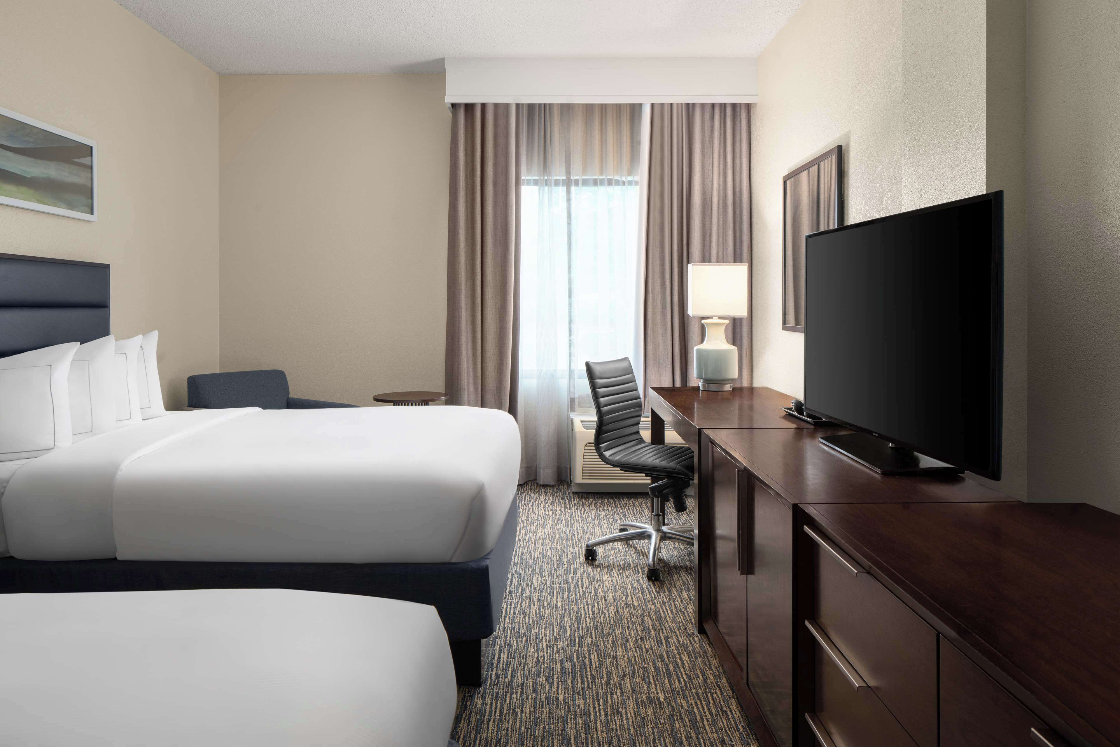 A hotel room with two beds, a desk with a TV, a chair, and a lamp.
