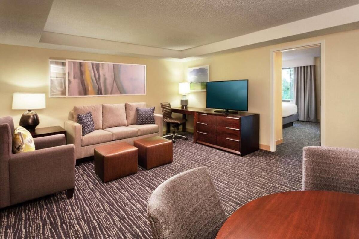 A hotel room with a sofa, armchairs, a TV, a desk, and a dining table.
