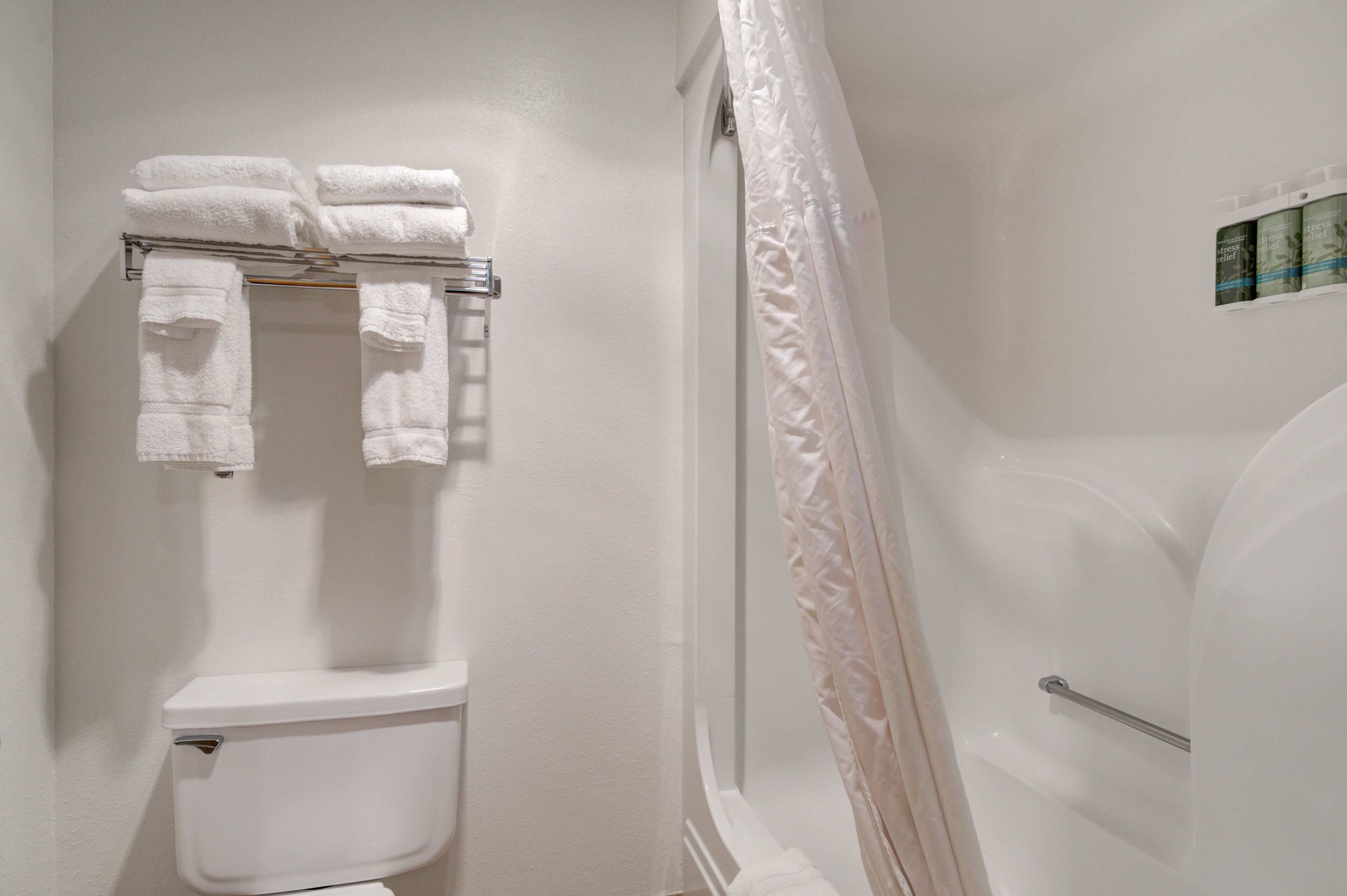 A bathroom with a toilet, a towel rack with folded towels, and a shower curtain.