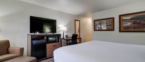 A hotel room with a bed, a desk, a chair, a TV, and a refrigerator.