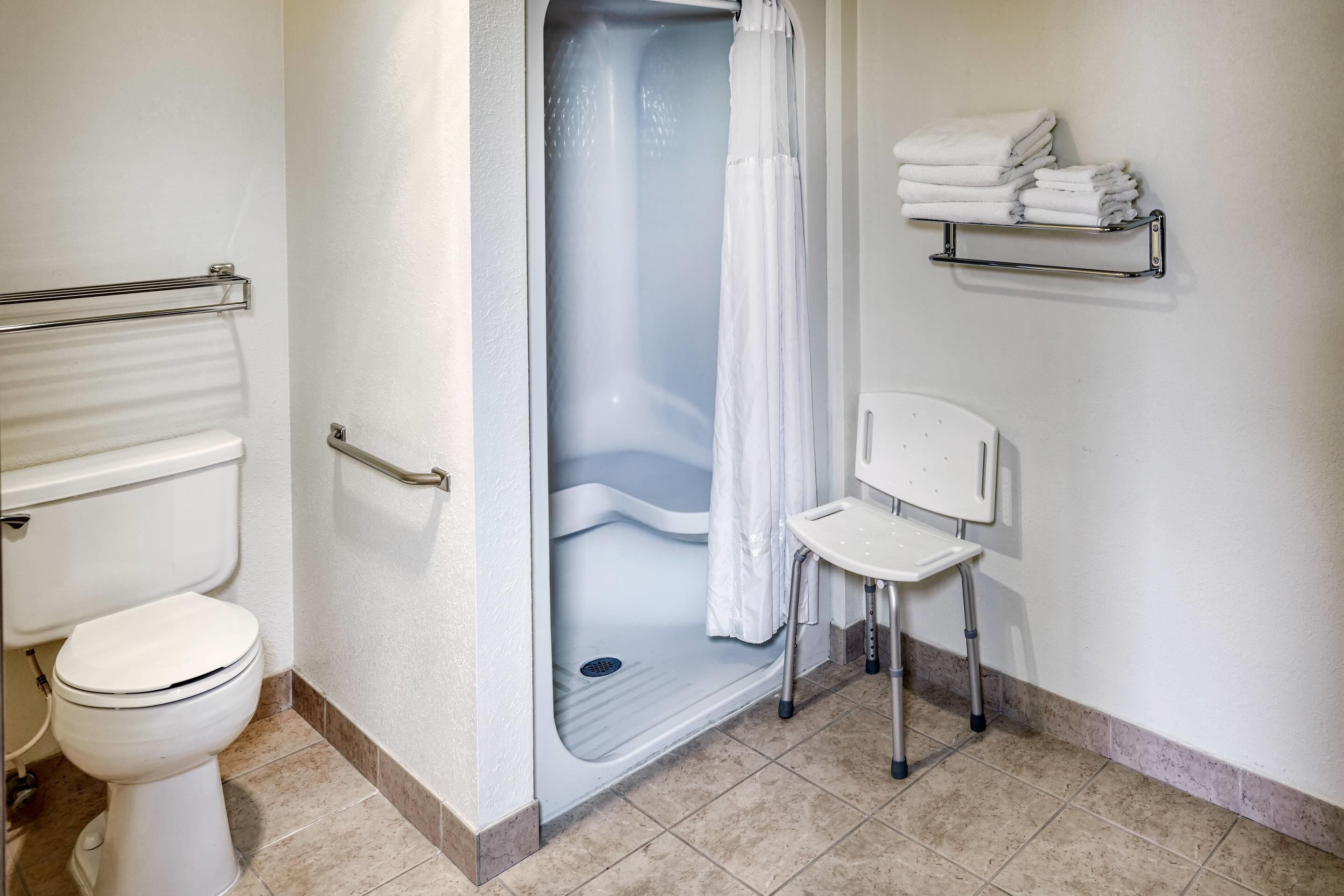 A bathroom with a shower, toilet, and a chair.