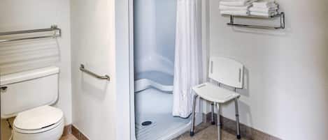 A bathroom with a shower, toilet, and a chair.