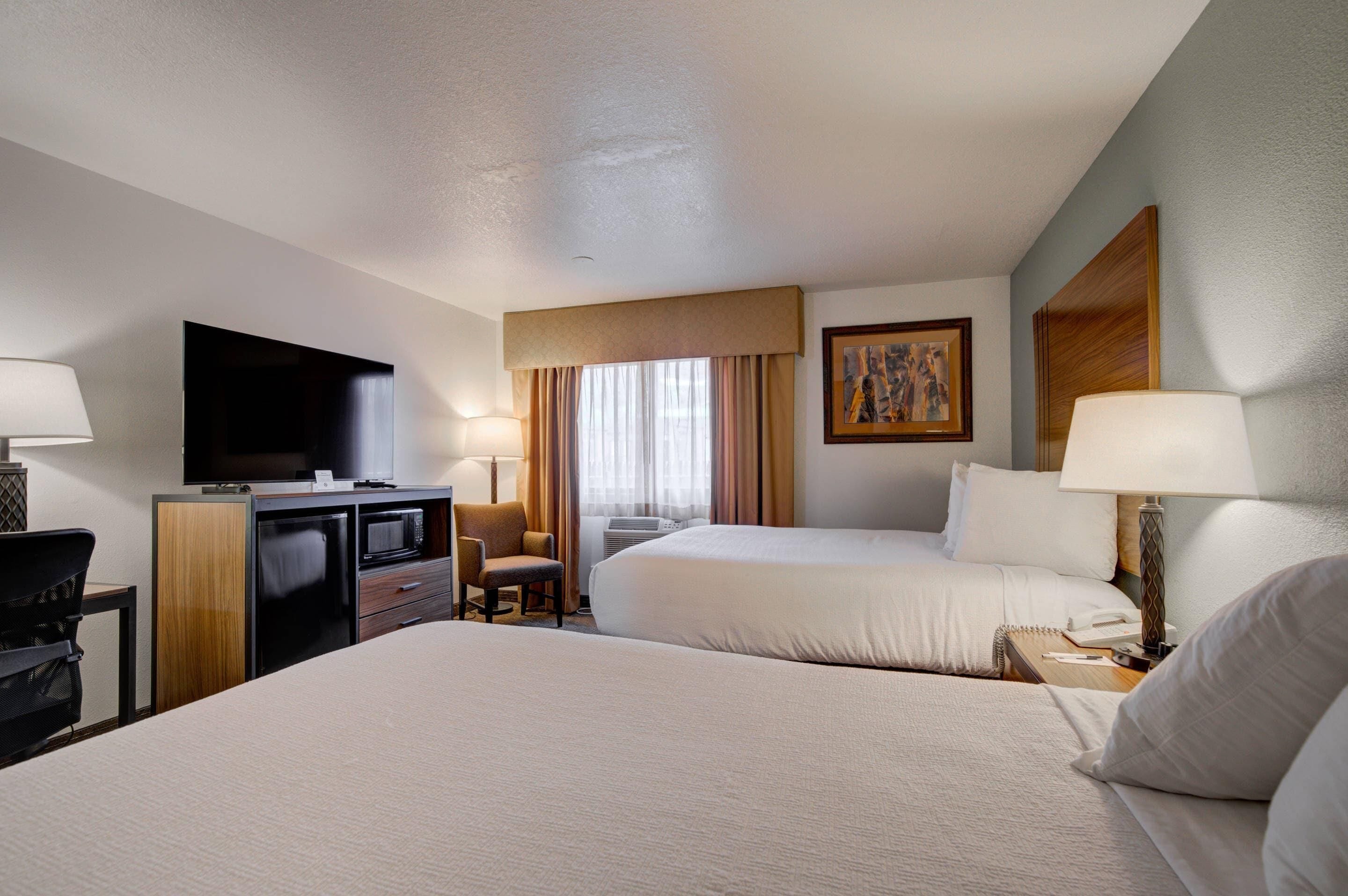 A hotel room with two beds, a desk with a TV, a chair, a lamp, and a painting on the wall.