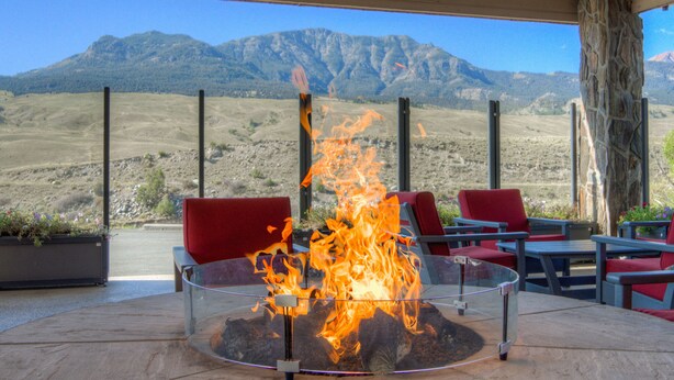 Un foyer extérieur avec vue sur les montagnes, des chaises rouges et un pilier en pierre.