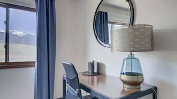 A hotel room with a desk, chair, lamp, and a large window with curtains.