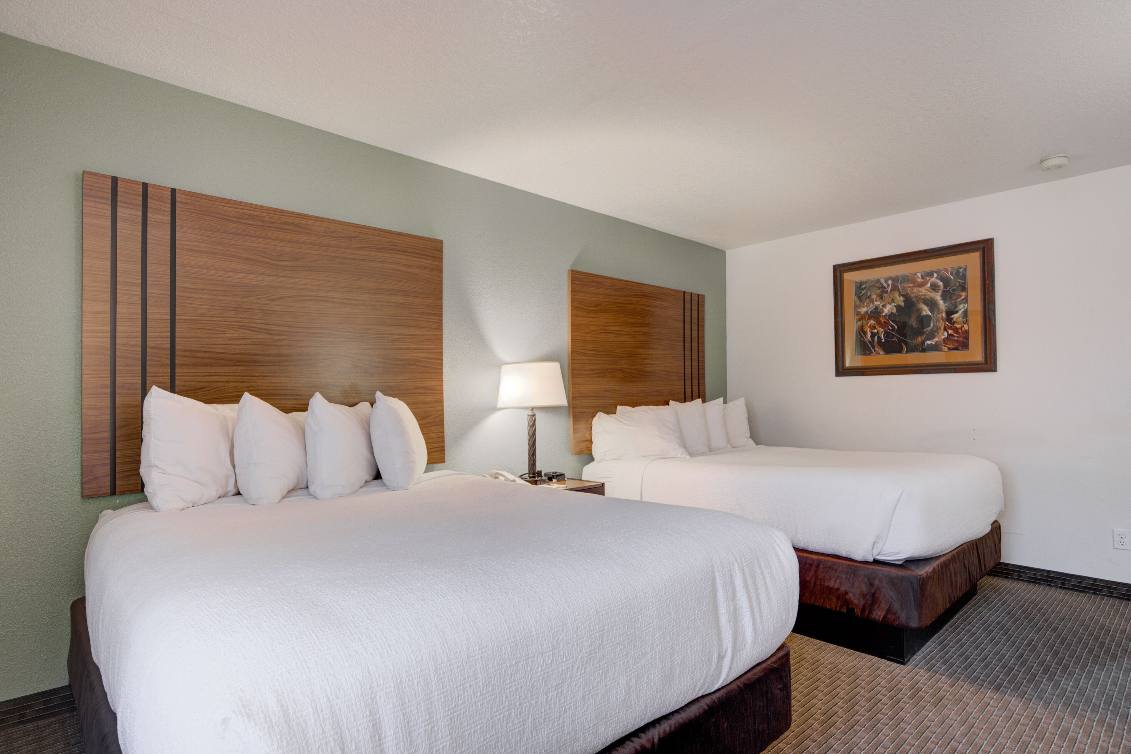 A hotel room with two beds, a nightstand, a lamp, and a framed picture on the wall.