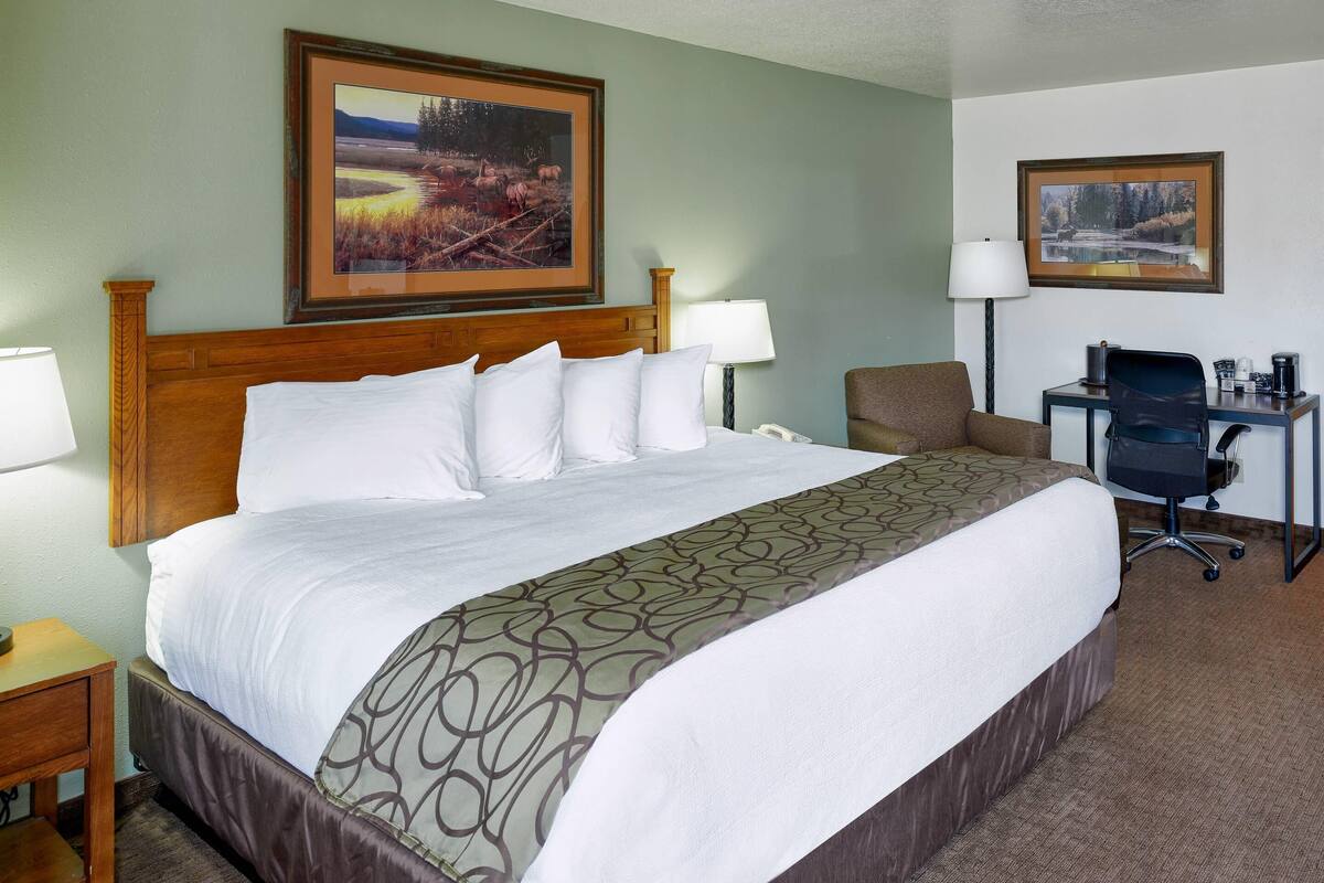 A hotel room with a large bed, a desk with a chair, two lamps, and framed pictures on the walls.