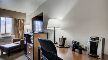 A hotel room with a desk, a chair, a television, a lamp, a coffee maker, and a window with curtains.