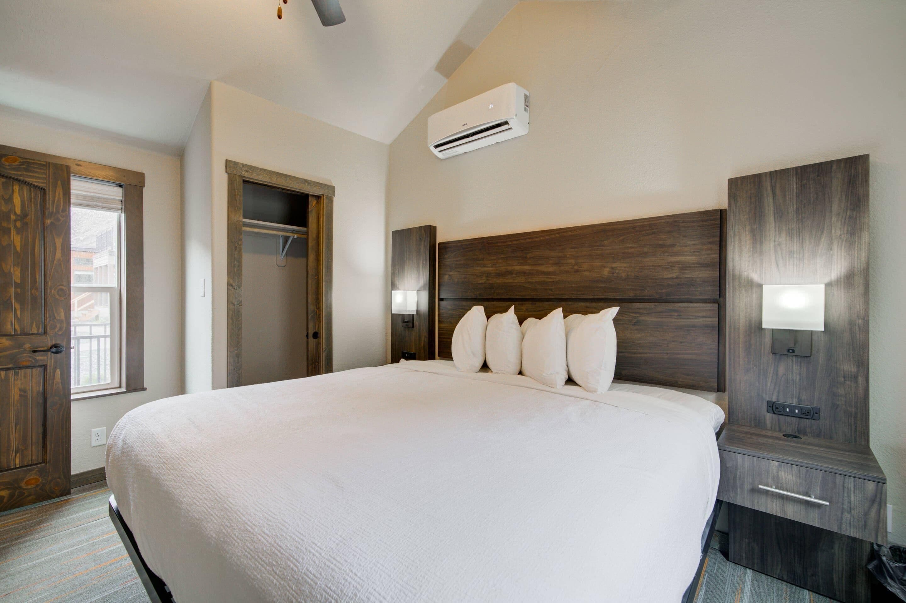Una cama grande con cabecera de madera, una mesita de noche con lámpara y un aire acondicionado instalado en la pared.