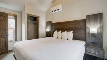 Una cama grande con cabecera de madera, una mesita de noche con lámpara y un aire acondicionado instalado en la pared.