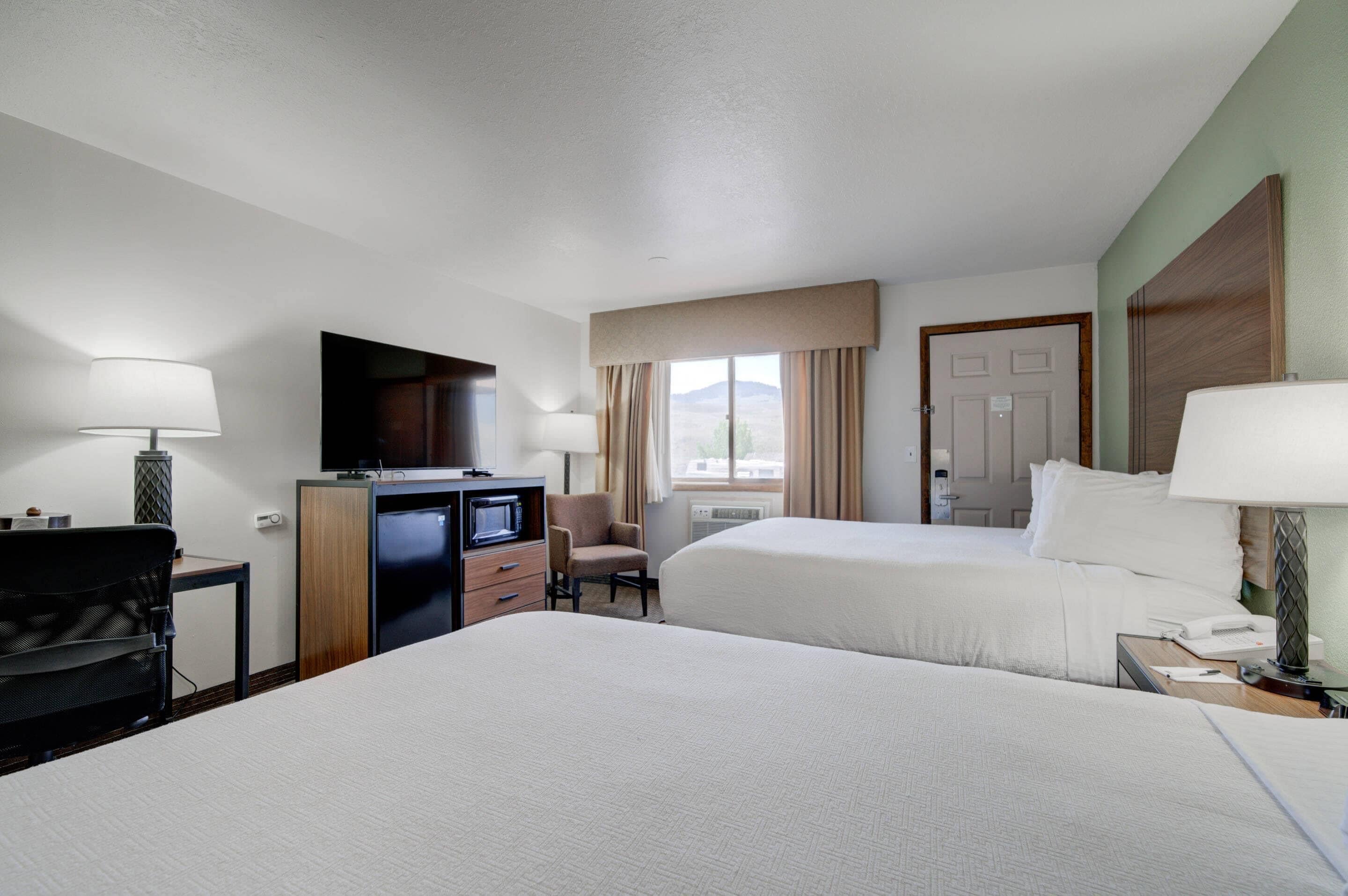 Habitación de hotel con dos camas, un escritorio con computadora, una silla y un televisor.