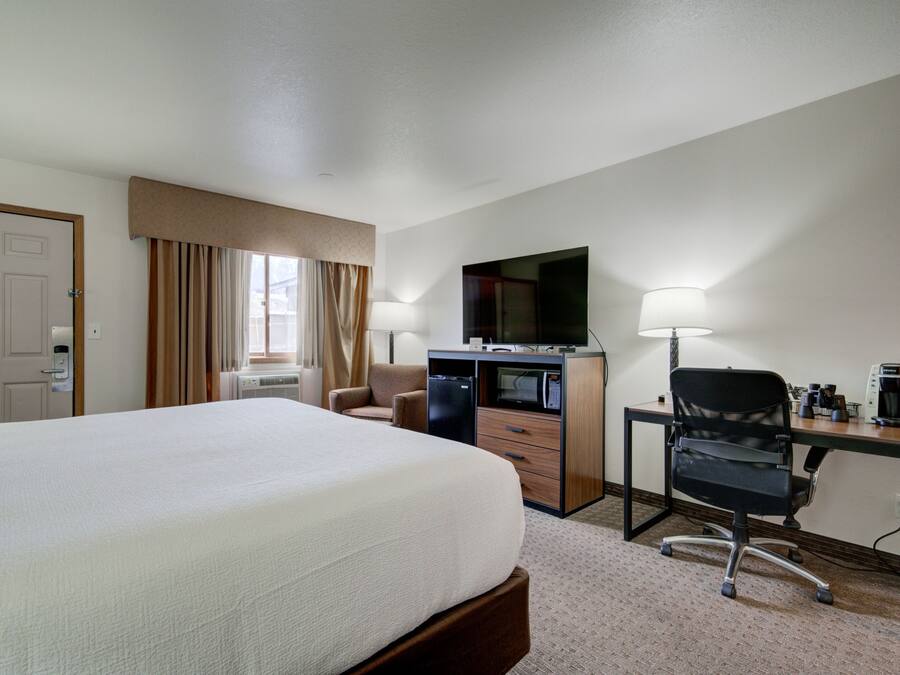 A hotel room with a large bed, a desk with a computer, a chair, a television, and a coffee maker.