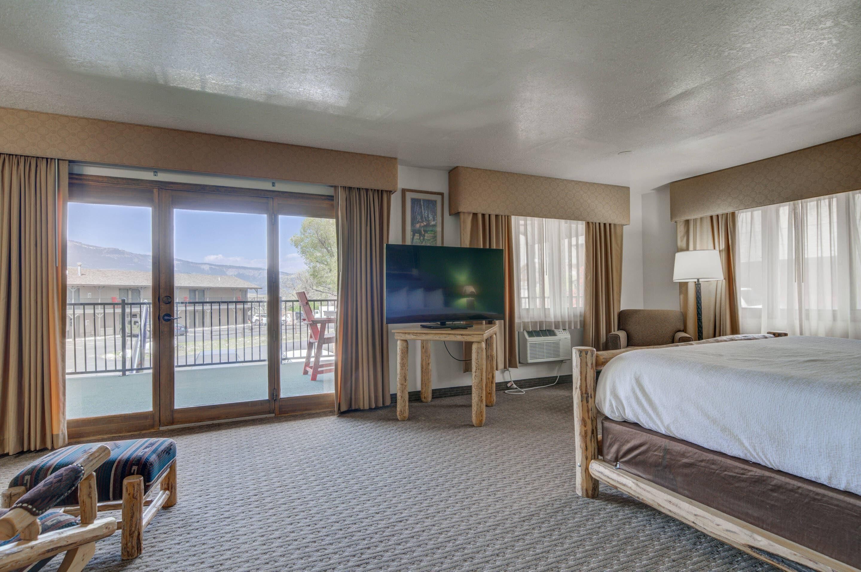 A hotel room with a large bed, a television on a wooden stand, a chair, and a view of the outdoors through a sliding door.