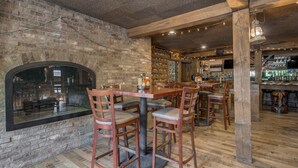 Un intérieur rustique avec des murs en briques, des planchers en bois et un coin bar doté d’étagères remplies de bouteilles.