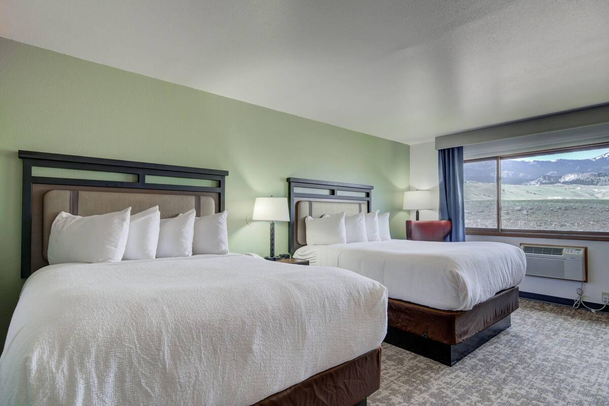 A hotel room with two beds, a large window with a mountain view, and a carpeted floor.