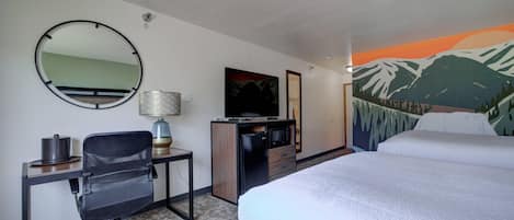 Quarto de hotel com cama, escrivaninha, cadeira, televisão e pintura de montanhas.