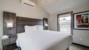 A hotel room with a large bed, a nightstand with a lamp, an air conditioning unit, and a poster on the wall.