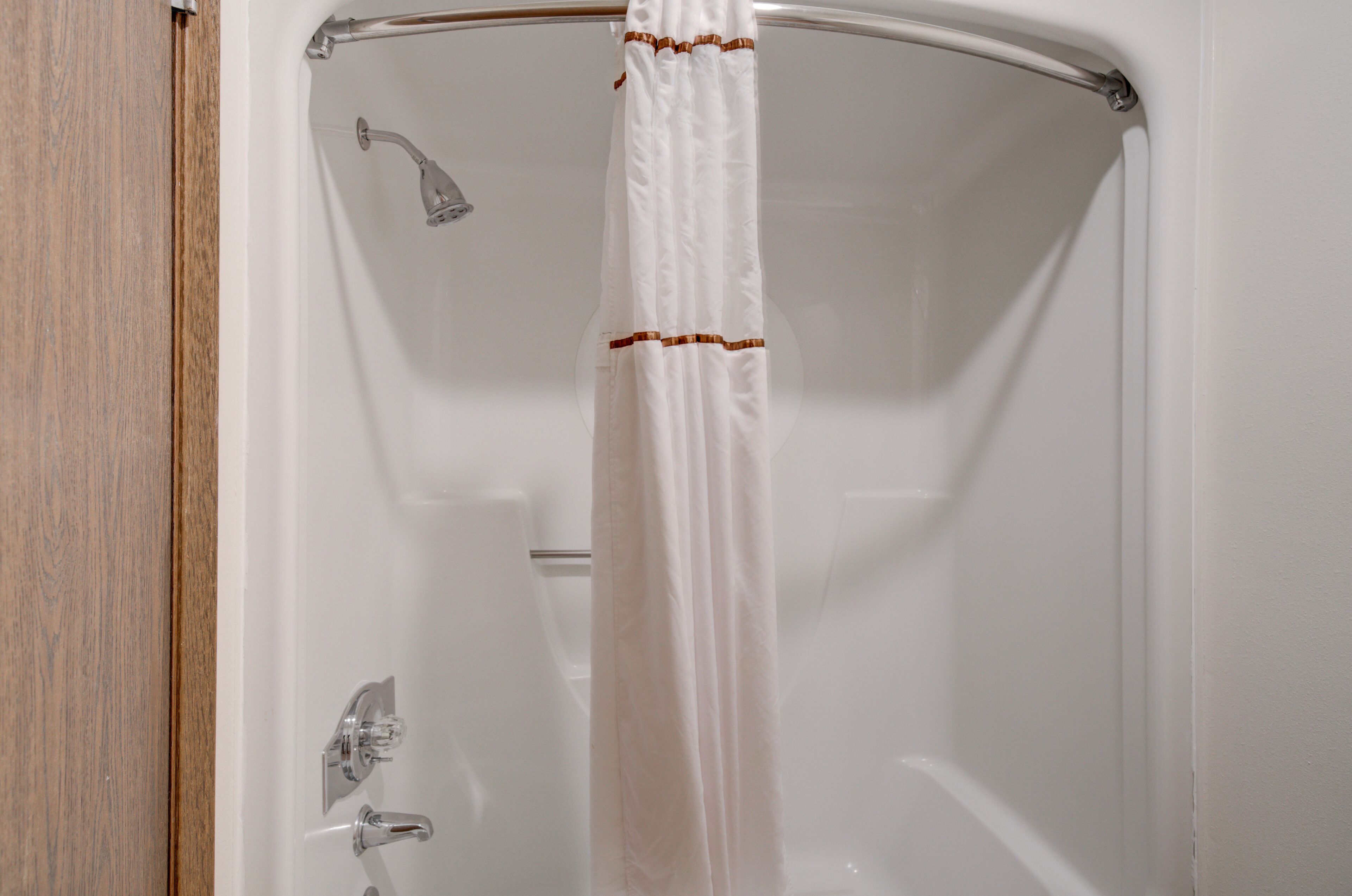 Ducha con cortina blanca y cabezal de ducha cromado.