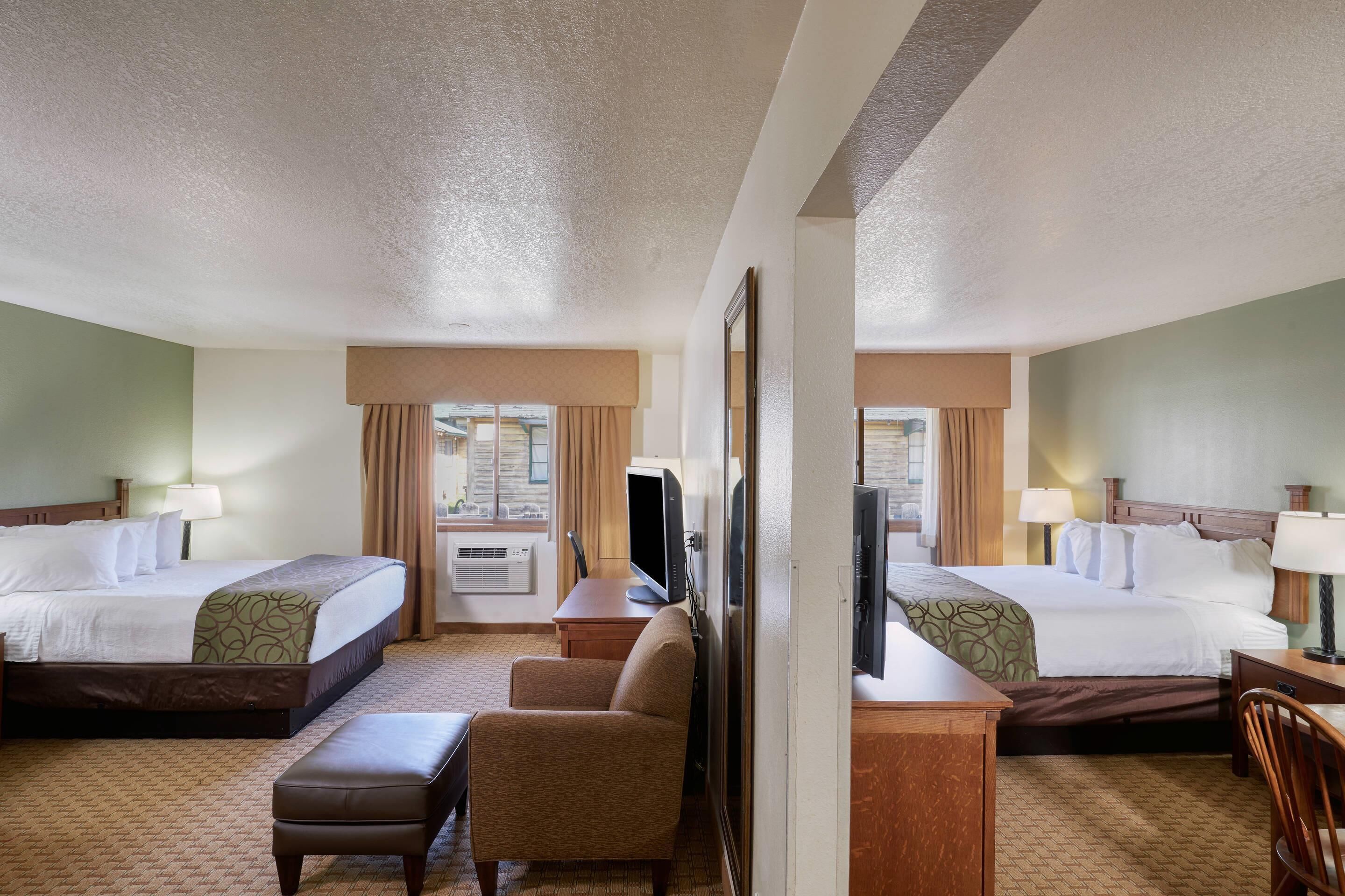 A hotel room with two beds, a desk, a chair, a TV, and a window with curtains.