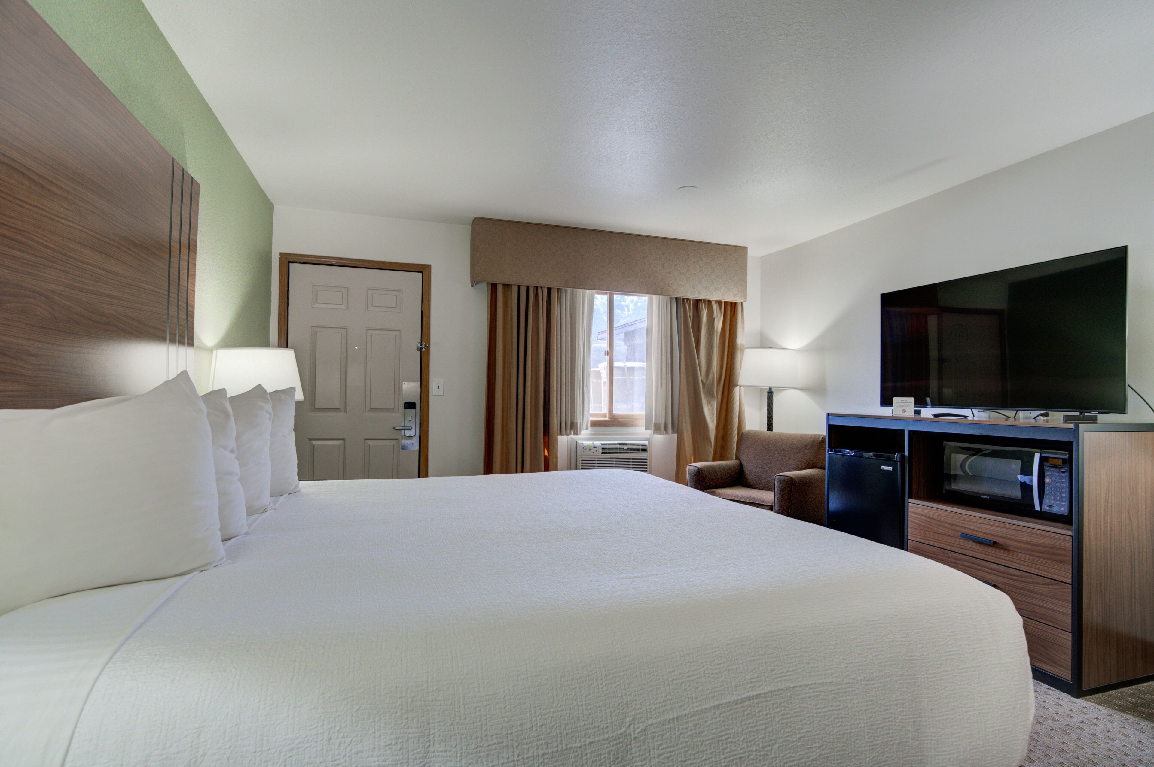 Habitación de hotel con una cama grande, un escritorio con microondas, un televisor y una puerta.