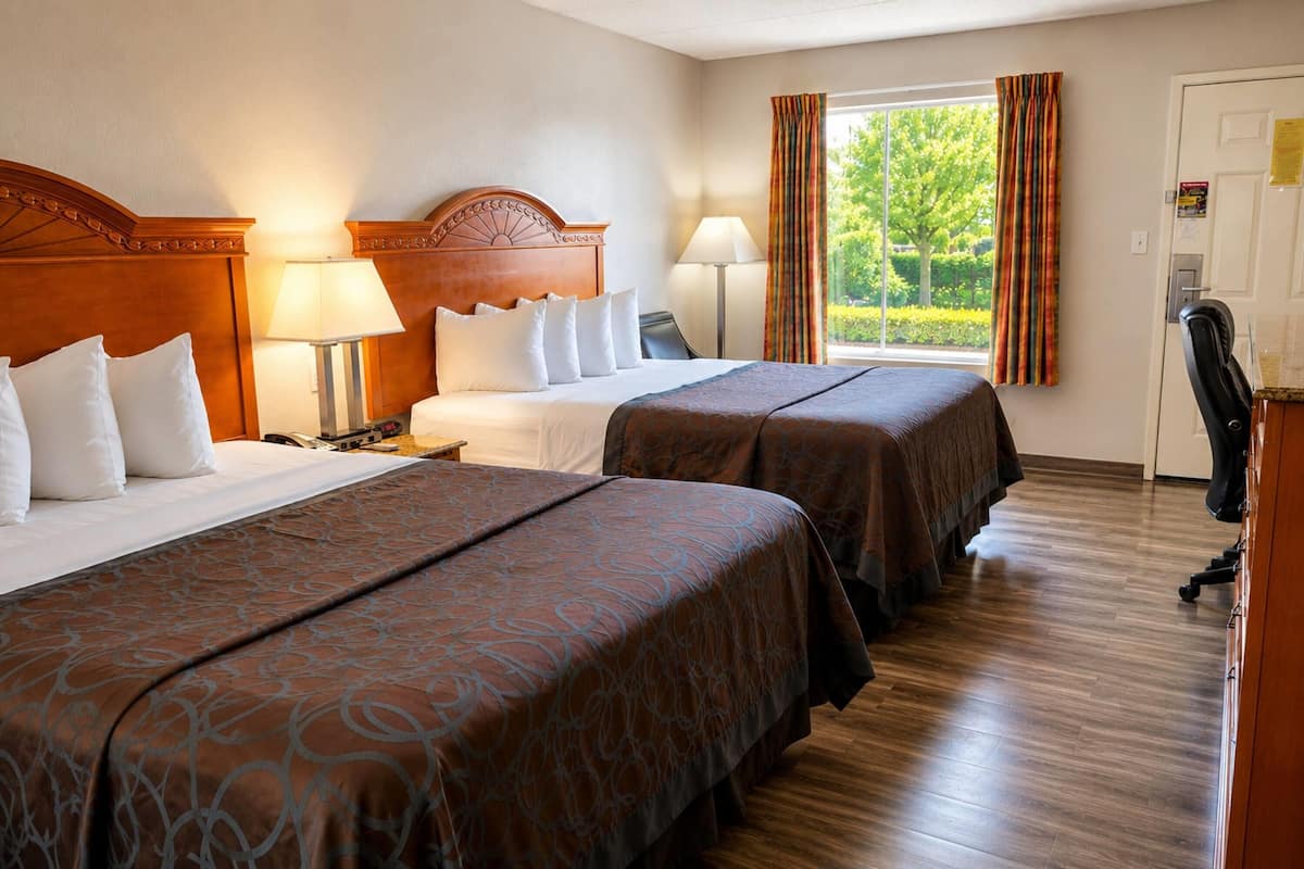 A hotel room with two beds, a desk, a chair, and a window with curtains.