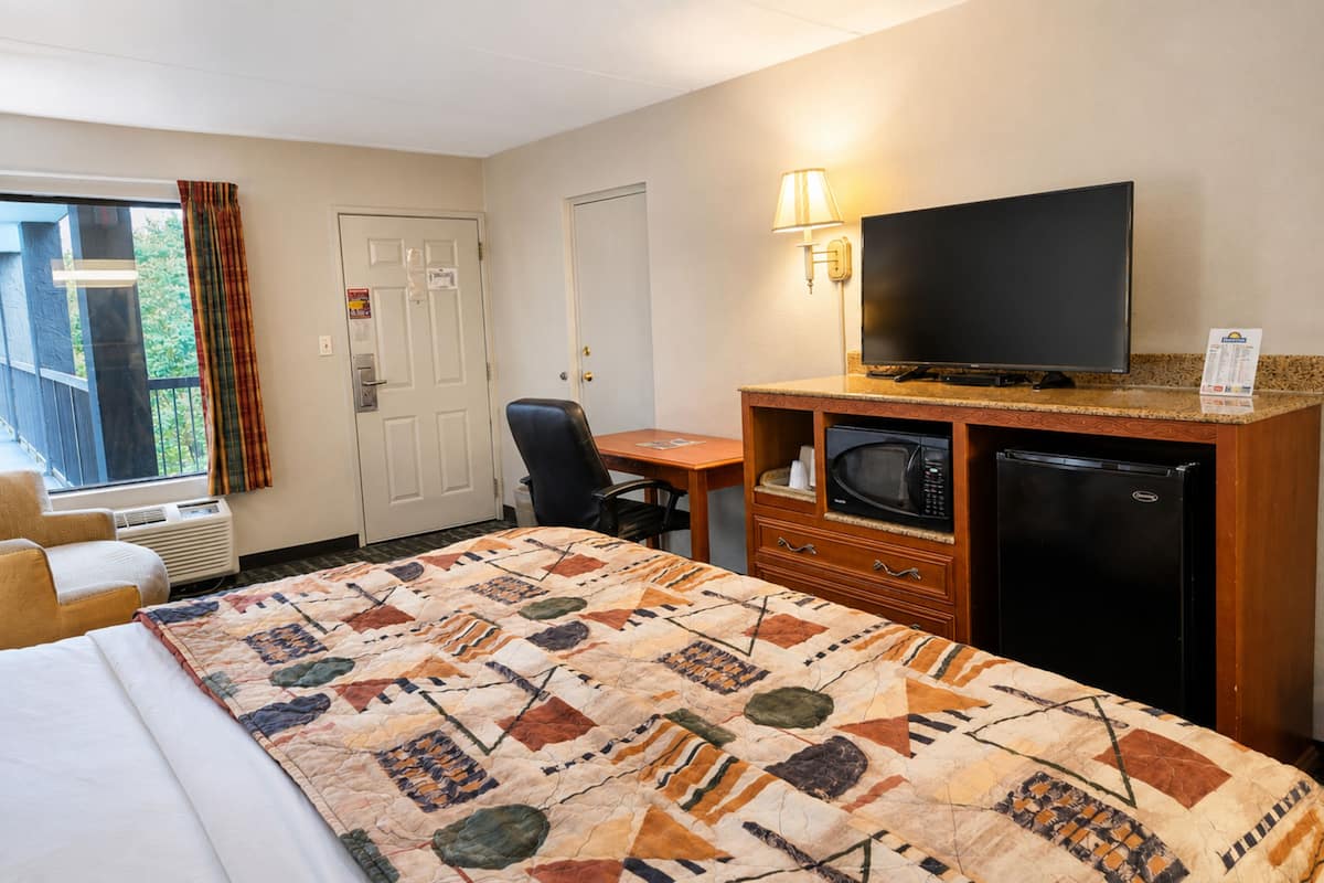 A hotel room with a bed, a desk, a television, a microwave, and a refrigerator.
