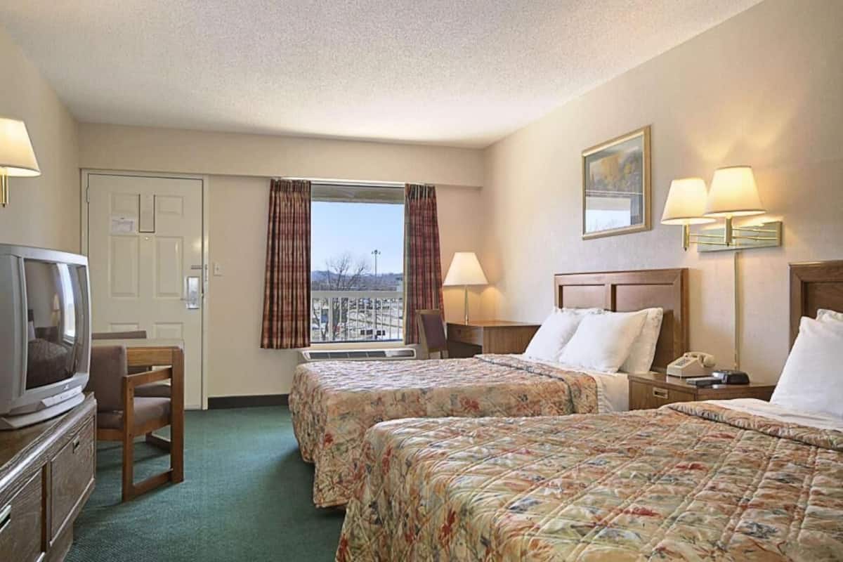 A hotel room with two beds, a television, a desk, and a window with curtains.