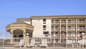 A multi-story motel with a flat roof, balconies, and a covered area with lounge chairs.