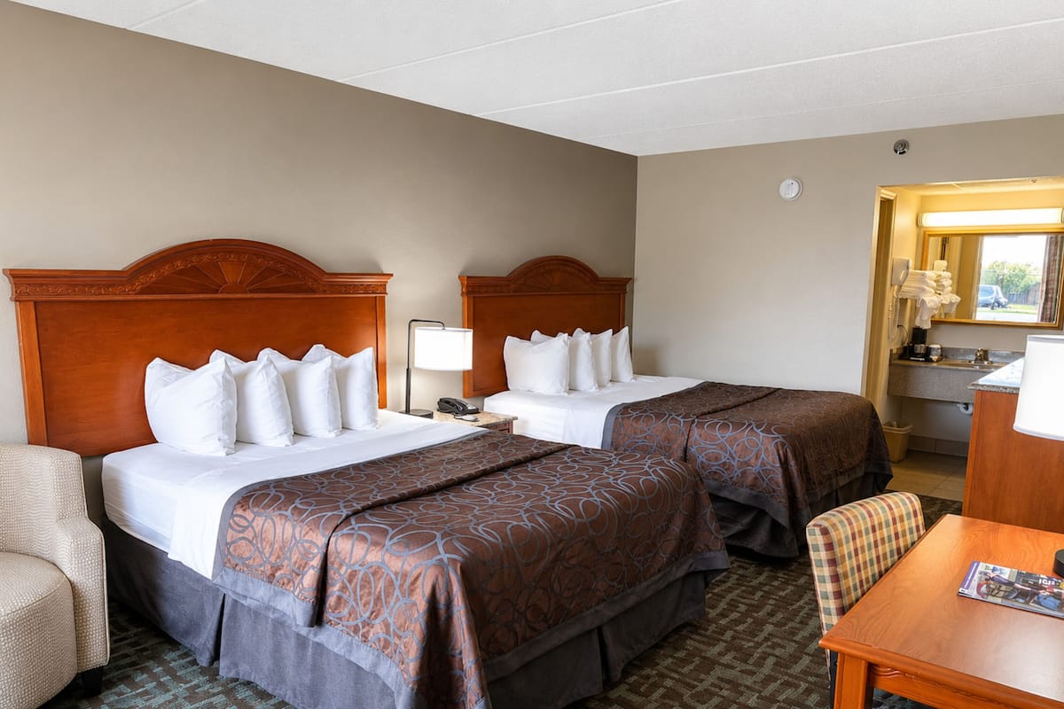 A hotel room with two beds, a desk, a chair, and a bathroom visible through an open door.