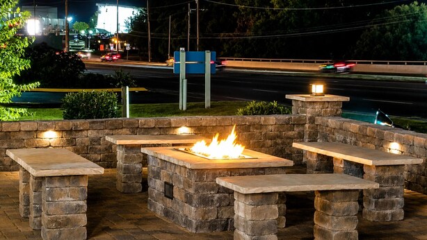 Outdoor stone benches with a central fire feature, surrounded by a brick wall.