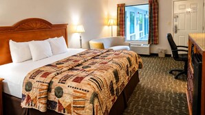 A hotel room with a large bed, a desk, a chair, a window with curtains, and a door.