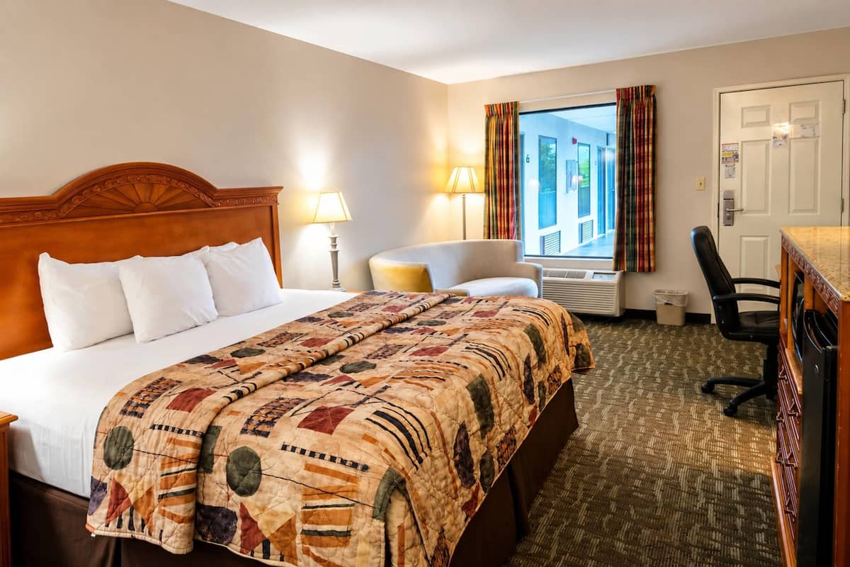 A hotel room with a large bed, a desk, a chair, a window with curtains, and a door.