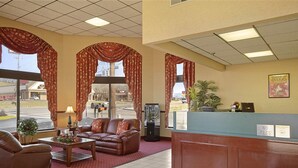 A hotel lobby with a reception desk, leather sofas, a coffee table, a lamp, a potted plant, and large windows.
