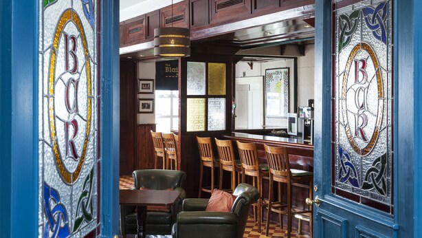A bar area with wooden chairs, a bar counter, and stained glass windows with the word "BORN". - Park Inn by Radisson Shannon Airport (Shannon)