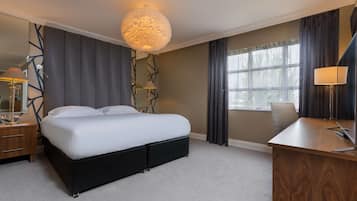 A hotel room with a large bed, a desk, a chair, a lamp, and a large window with curtains.