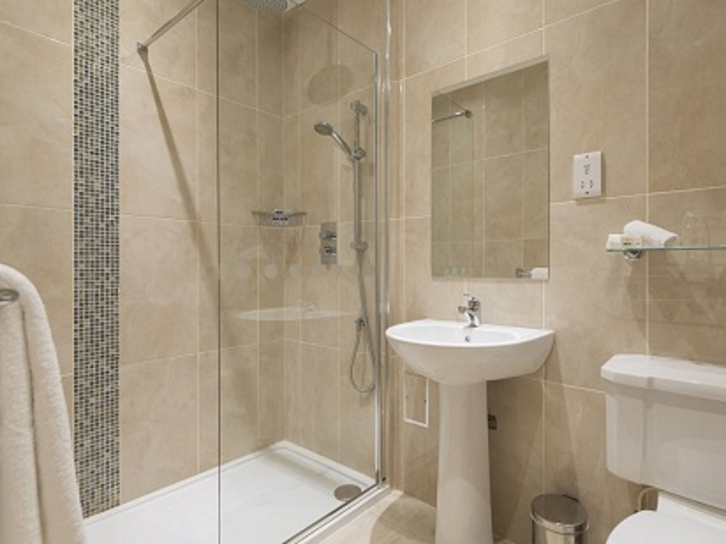 Et moderne badeværelse med et glasafskærmet brusebad, en væghængt håndvask og et toilet.