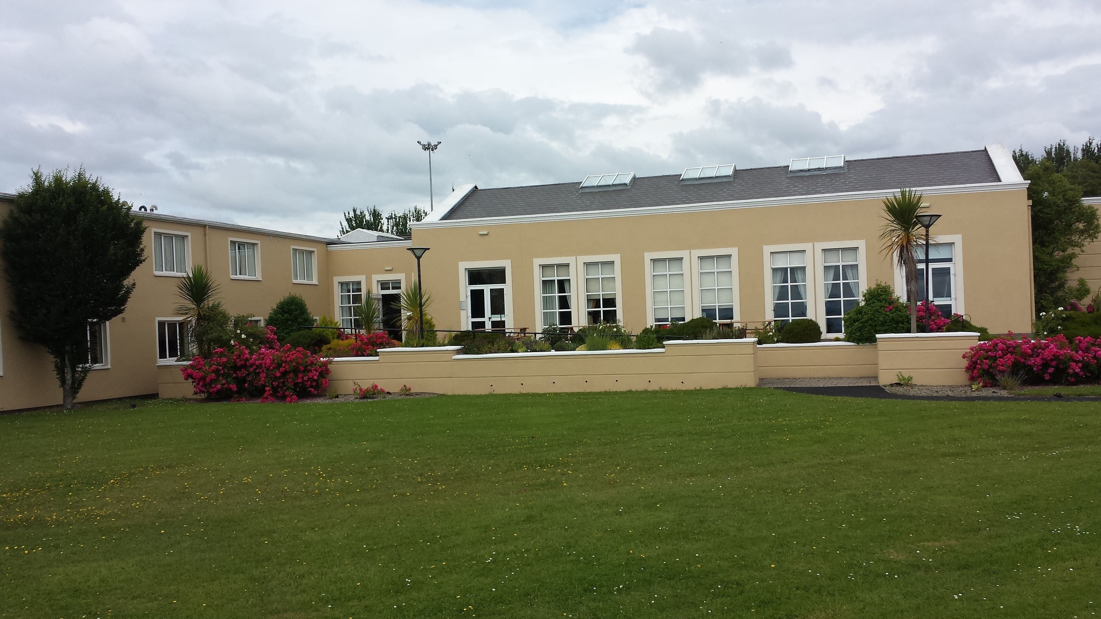 A two-story building with a flat roof, multiple windows, and a well-maintained lawn with scattered flowers.