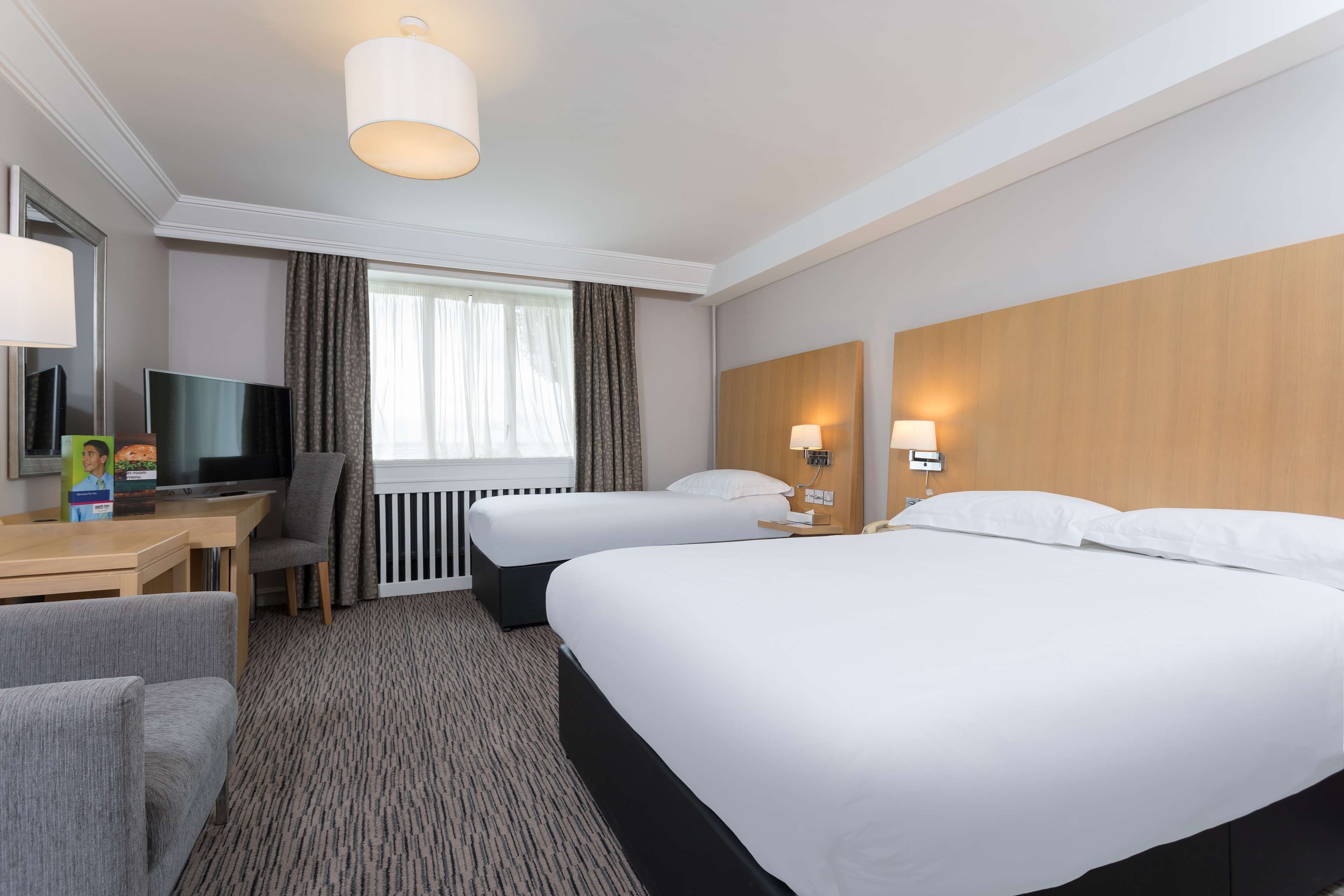 Ein Hotelzimmer mit zwei Betten, einem Schreibtisch mit Computer, einem Fernseher und einem Fenster mit Vorhängen.