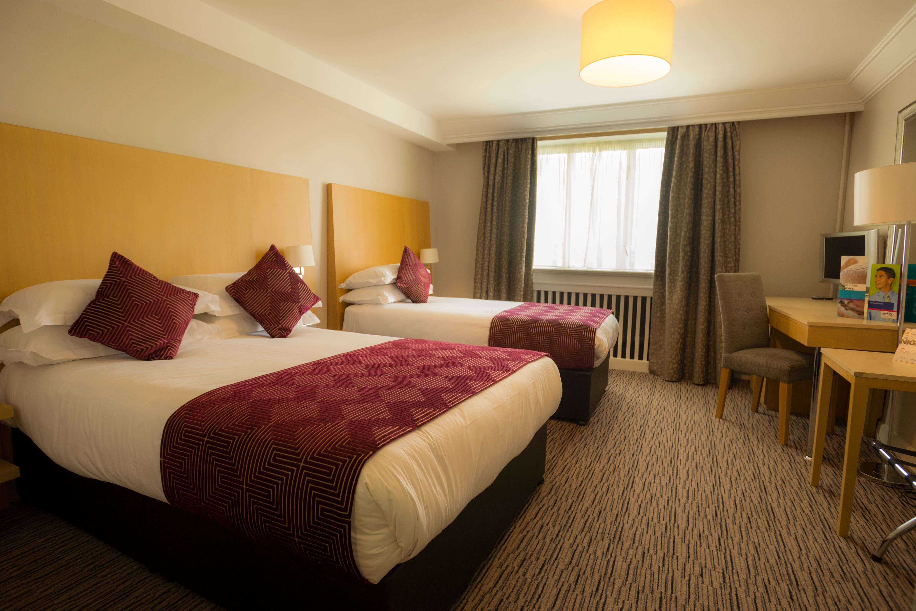 A hotel room with two beds, a desk, a chair, and a window with curtains.