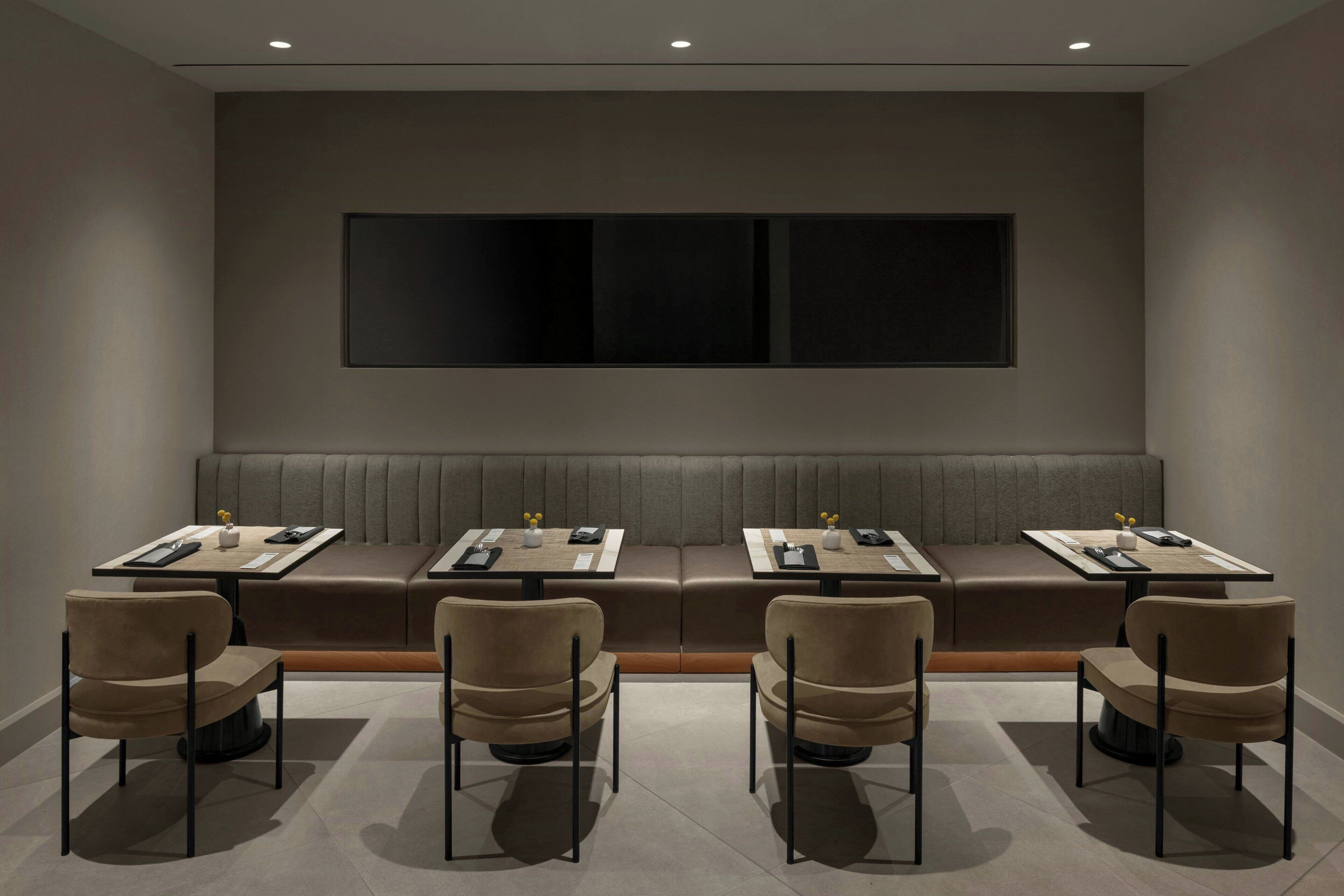 A modern hotel room with a sofa set, four chairs, and a large wall-mounted TV.