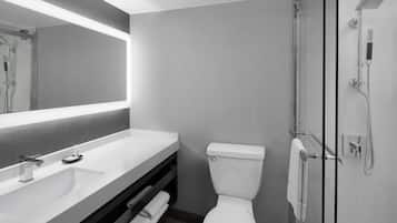A modern bathroom with a large mirror, a white sink, a toilet, and a glass-enclosed shower.