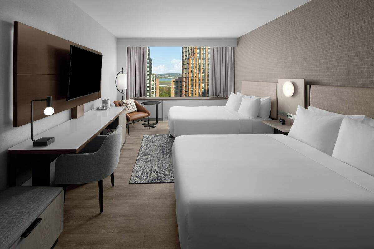 A hotel room with a large bed, a desk, a chair, a TV, and a view of the cityscape.