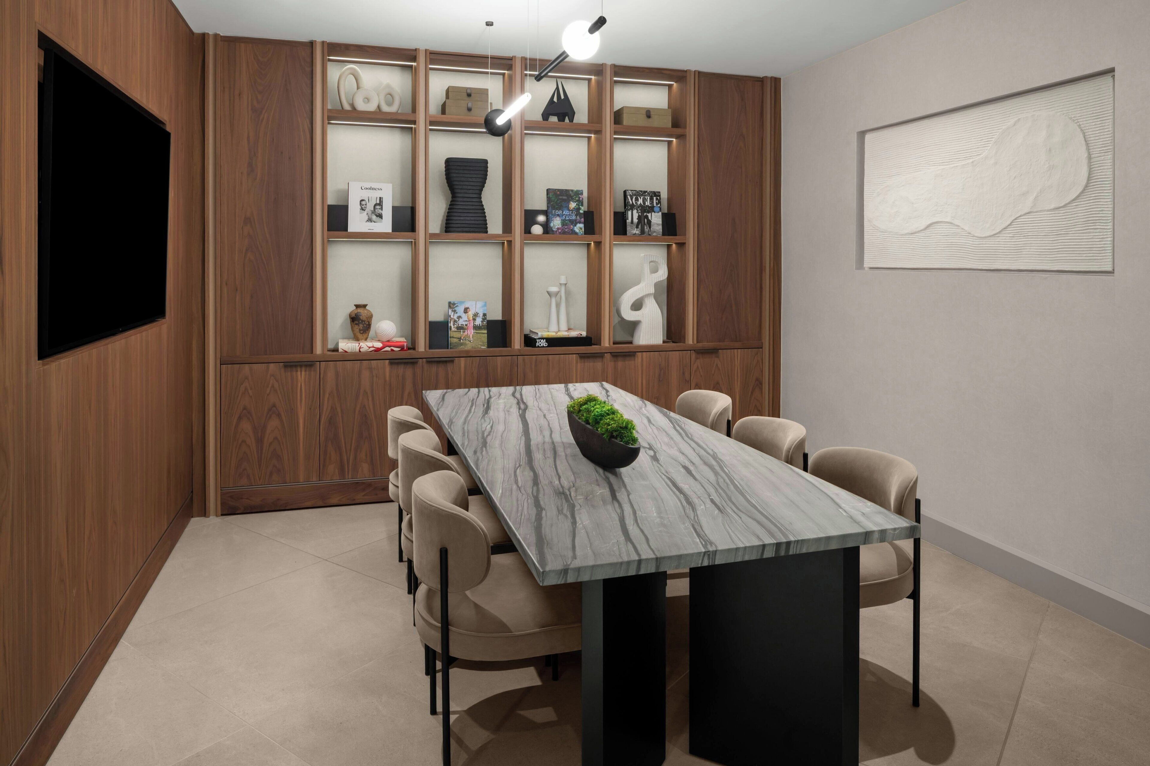 Un comedor moderno con una mesa de mármol, sillas color beige y una estantería de madera empotrada con objetos decorativos.