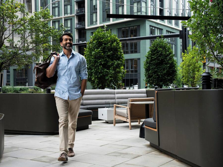 A man walking on a rooftop patio with outdoor seating and greenery.