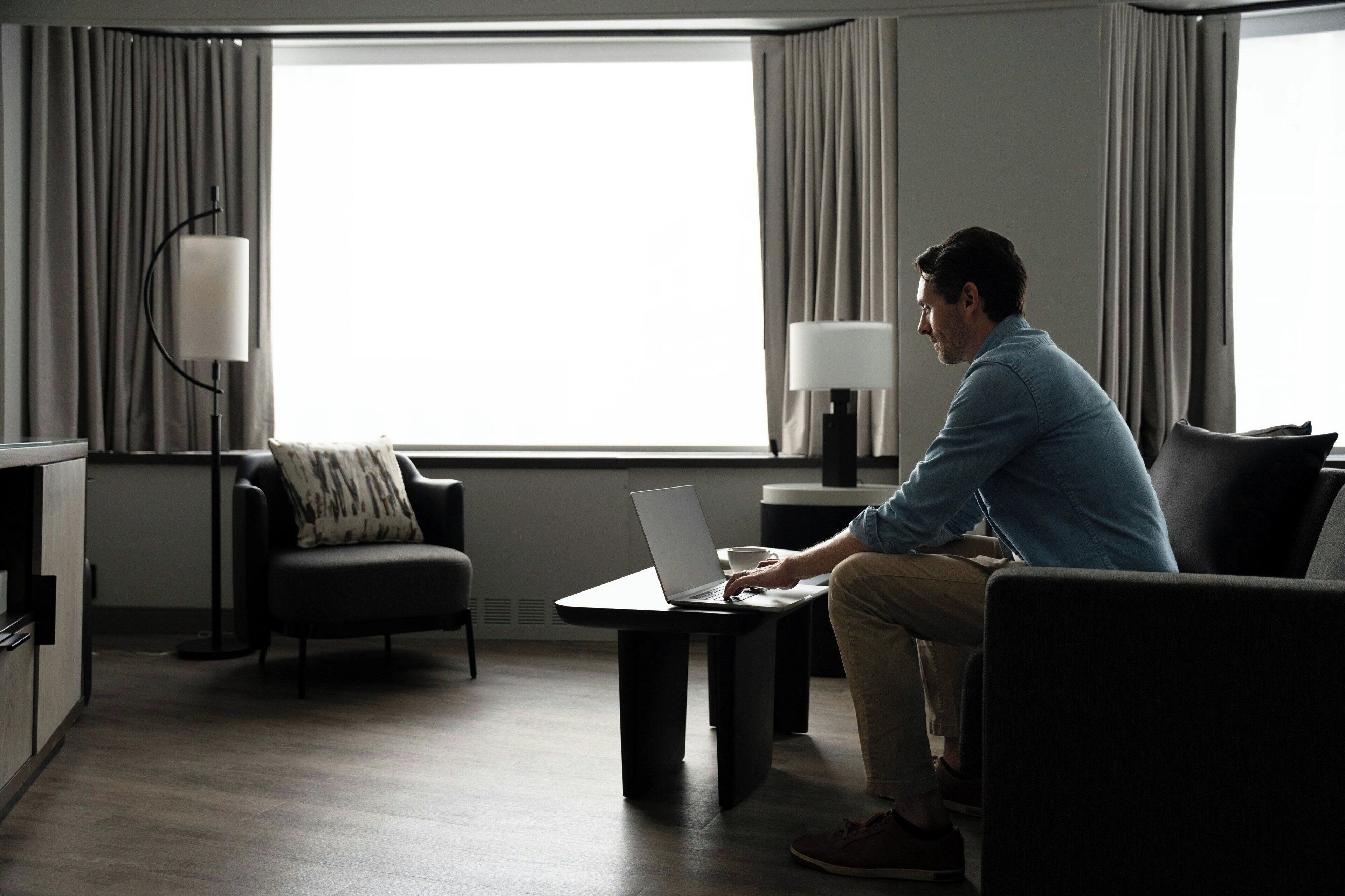 A modern living room with a large window, a sofa, a coffee table, and a lamp.