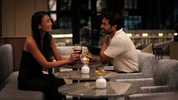 A couple seated at a round table in a dimly lit indoor setting, possibly a restaurant or lounge area, with a modern interior design and comfortable seating.